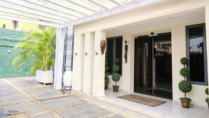 A covered outdoor area with a stone pathway leading to a building entrance, potted plants, and a green wall. - THE ATRIUM LAGOS (Lagos)