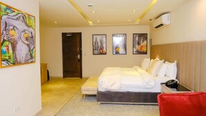 A hotel room with a bed, a bedside table with a phone, a red chair, and a door leading to another room. - THE ATRIUM LAGOS (Lagos)