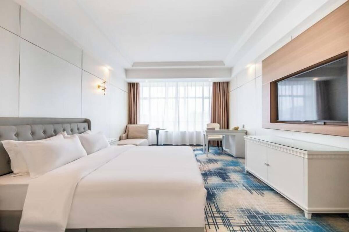 Une chambre d’hôtel avec un grand lit, un bureau, une télévision et une fenêtre avec des rideaux.
