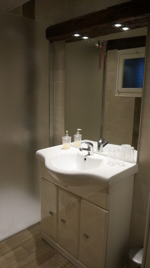 Une salle de bain avec un lavabo blanc, deux distributeurs de savon, un miroir et une petite fenêtre.