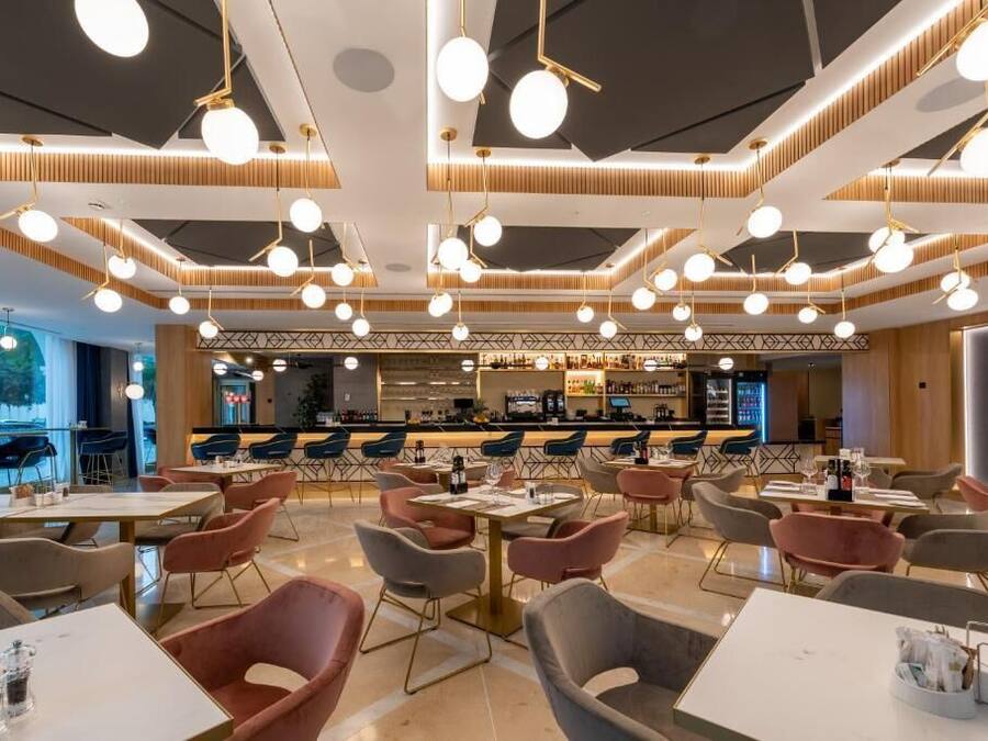 A modern restaurant interior with multiple dining tables and chairs, a bar area, and pendant lighting.
