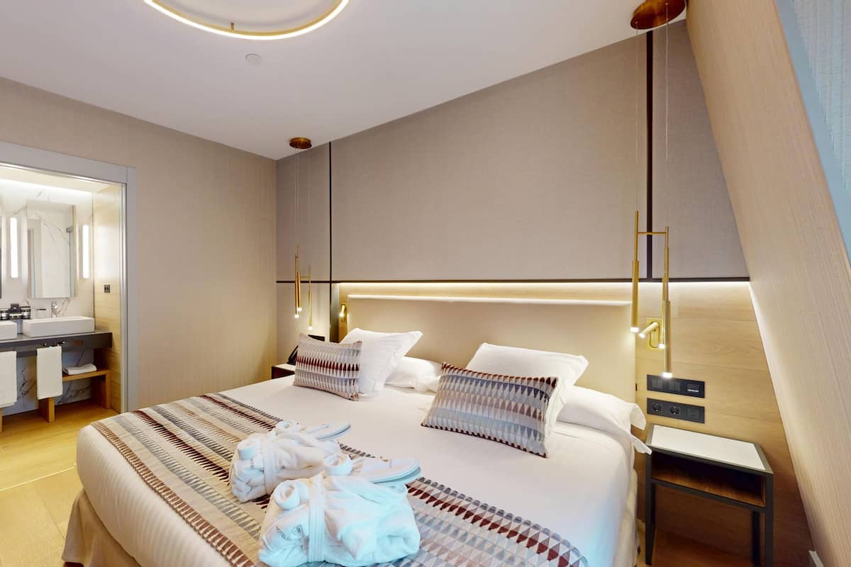 Een moderne hotelkamer met een groot bed, nachtkastje, spiegel en een zichtbare badkamer achter een glazen wand.