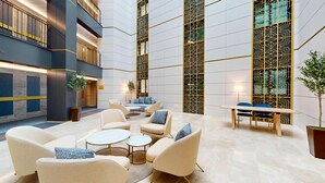 Een ruime lobby met een zithoek, een trap en een decoratieve wand.