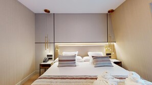 Una habitación de hotel moderna con una cama grande, mesitas de noche, un teléfono y una bata sobre la cama.
