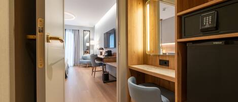 A modern hotel room with a wooden desk, a chair, a TV, and a minibar.