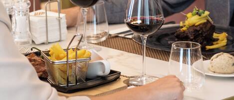 A dining table with a steak, fries, and a dessert, along with wine glasses and a basket of fruit.