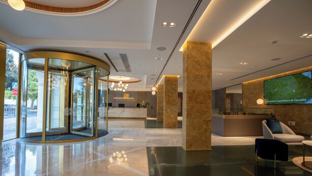 Een moderne hotellobby met een draaideur, een receptiebalie en een zithoek.
