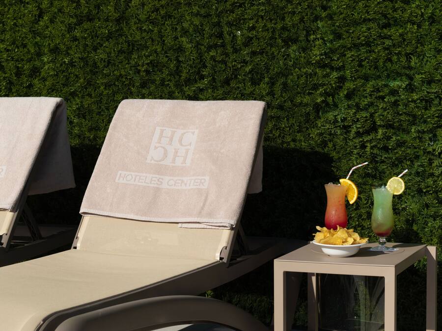 Two sun loungers with towels, a table with a drink and chips, and a hedge in the background.