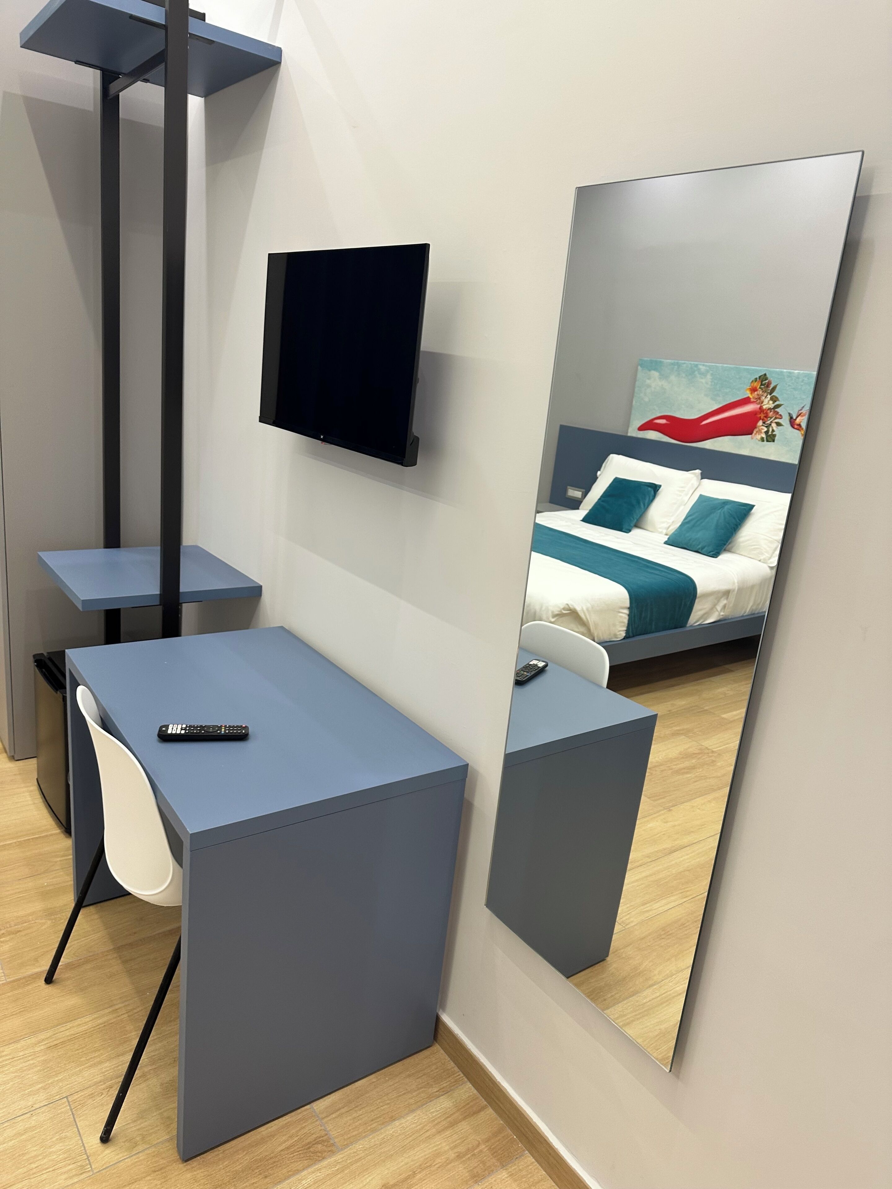 Una camera da letto moderna con un letto, una scrivania, una sedia, una televisione e un grande specchio.