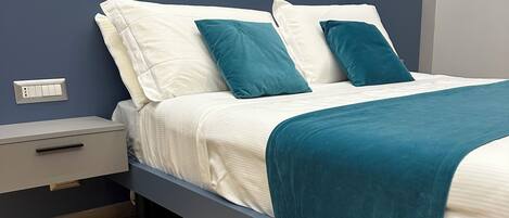 A modern bedroom with a bed, nightstand, and a wall-mounted power outlet.
