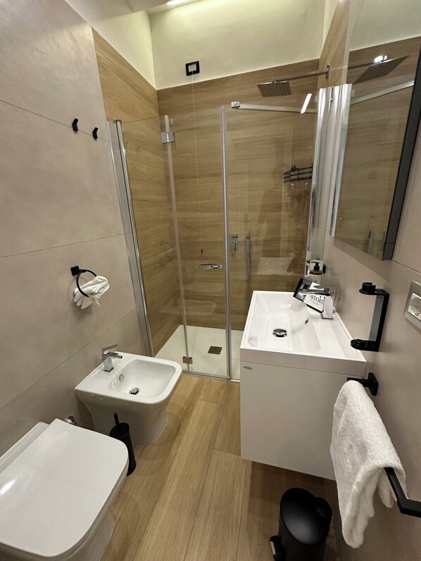A modern bathroom with a glass-enclosed shower, a white sink, and a bidet. - Astoria Napoli Centrale (Naples)