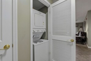 A laundry room with a washer and dryer, a door with a louvered panel, and a glimpse of a dining area in the background. - 2 BR | Sleeps 4 | Walk-in Shower | Jacuzzi | Mtn View (Pigeon Forge)