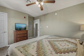A bedroom with a bed, a dresser, a television, a ceiling fan, and a door.