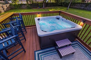 Un jacuzzi en una terraza de madera con cerco de madera, una mesa de madera y sillas azules.