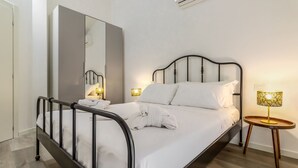A neatly made bed with white linens and a folded towel, a bedside lamp, and a mirror on the wall. - Sporting 1 64 by Wonderful Italy (Sirmione)