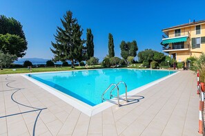 Una piscina rectangular con una escalera metálica, rodeada por una solana con baldosas.