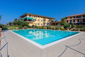 Una piscina rectangular con solárium empedrado, rodeada de edificios de varios pisos con balcones y un cielo azul despejado.