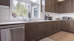 A modern kitchen with dark wood cabinets, a stainless steel dishwasher, a coffee maker, and a toaster.