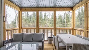 A wooden deck with a glass table and seating, overlooking a forest.