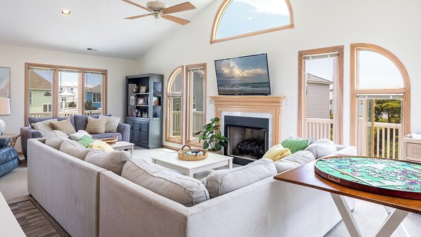 A spacious living room with a sectional sofa, a fireplace, a television, and large windows.