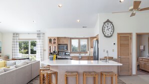 A modern kitchen with a central island, wooden stools, and a large clock on the wall.
