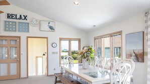 A dining area with a wooden table and white chairs, a vase with flowers, and artwork on the walls.