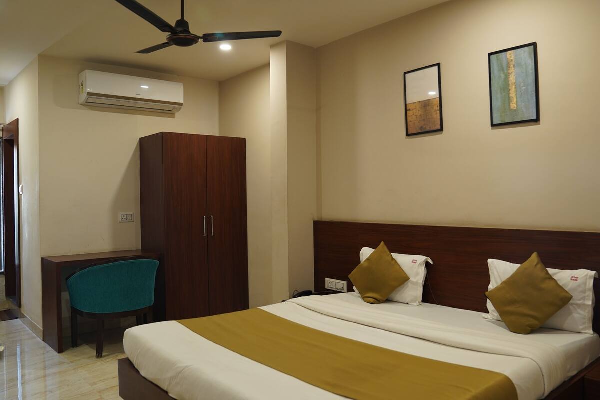 A hotel room with a bed, a desk, a wardrobe, and an air conditioning unit.