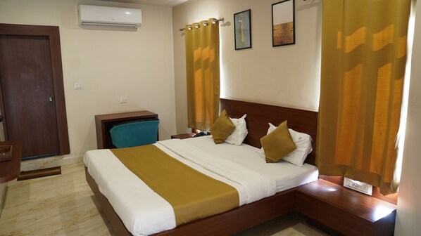 A hotel room with a bed, a desk, an air conditioner, and a door. - hotel urban house (Bhopal)