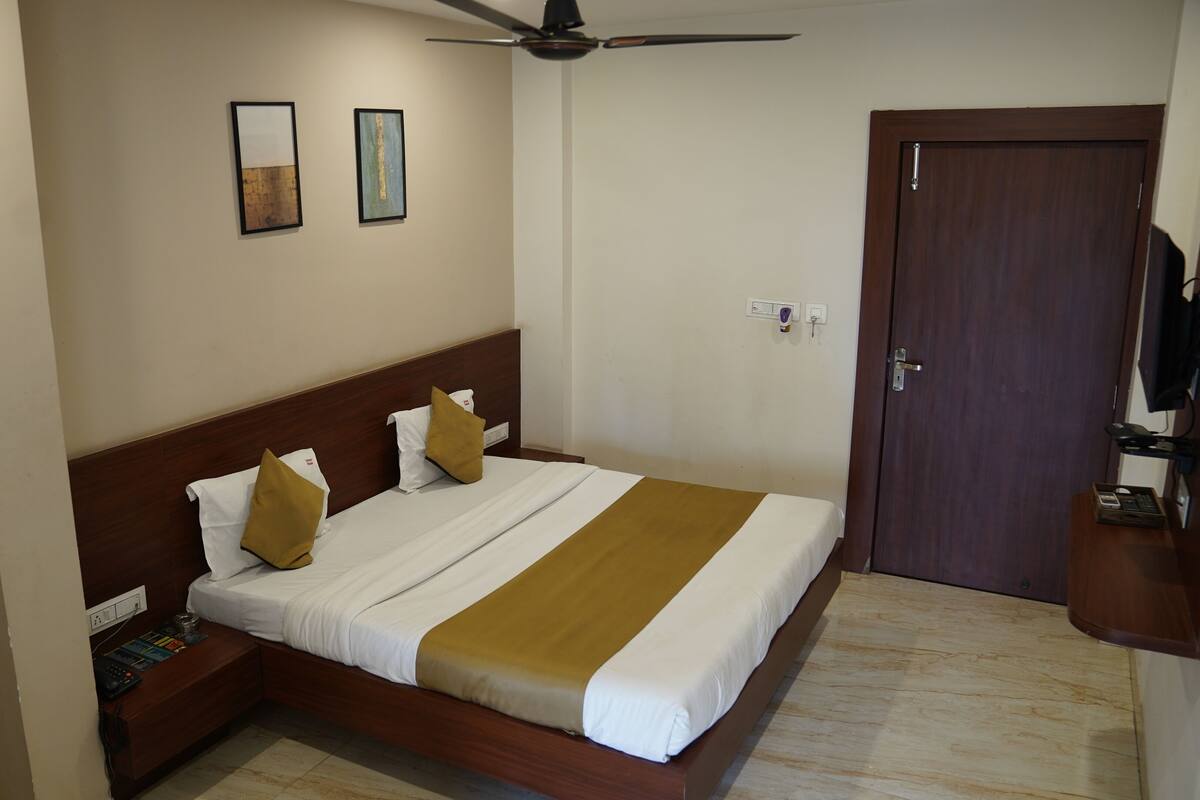 A hotel room with a wooden bed, white and brown bedding, a ceiling fan, and a door with a TV on a stand.