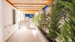Een overdekte buitenpassage met een houten plafond, witte wanden en een plantenbak met groene planten.