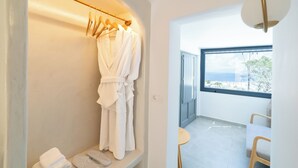 Een moderne badkamer met een witte badkuip, een handdoekrek met een witte badjas, en uitzicht op zee door een groot raam.