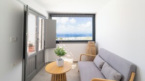 Een balkon met uitzicht op zee, een grijze bank, een houten tafeltje met een plant en een gevlekte vaas.