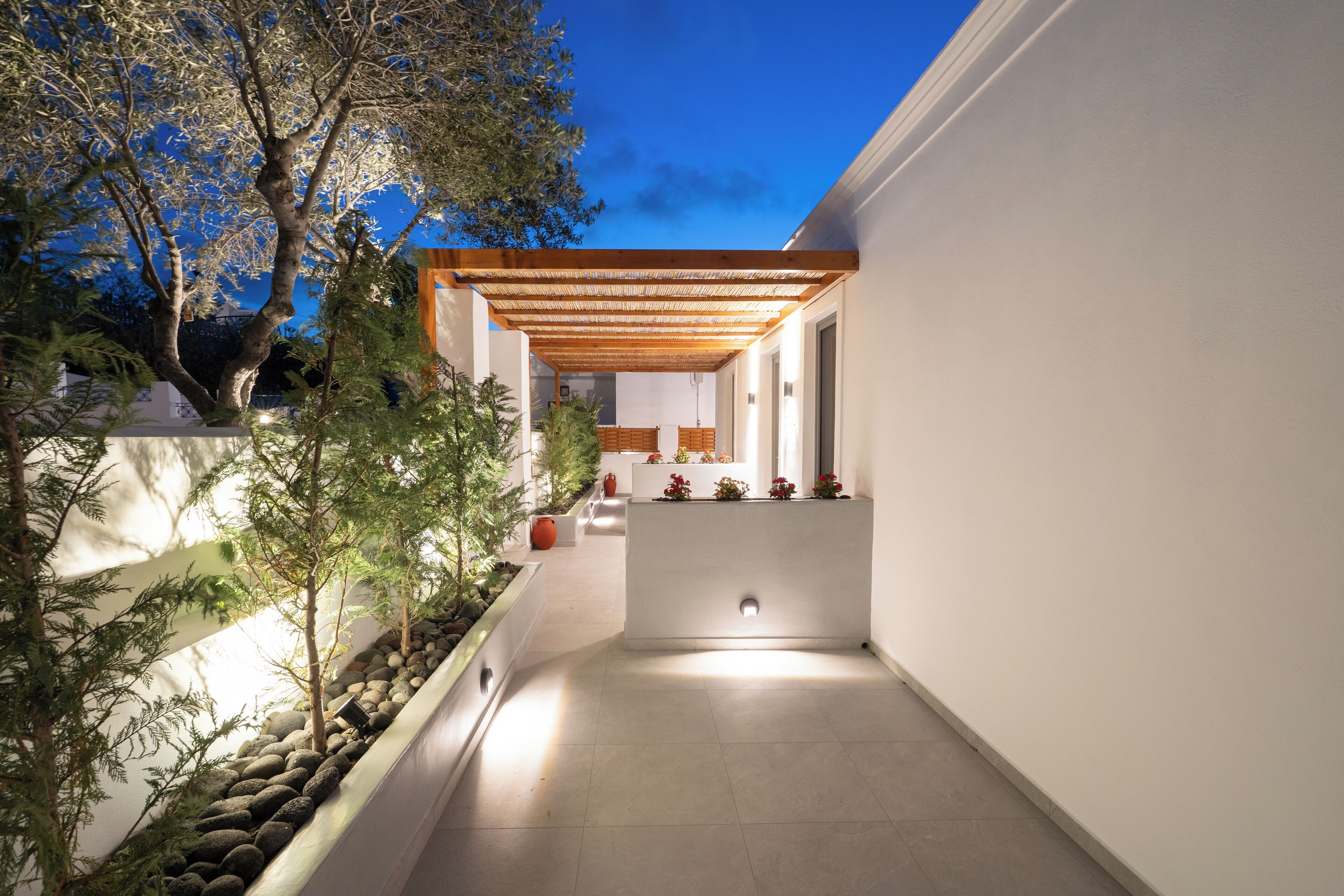 Eine moderne Außenpatio mit einer Holz-Pergola, einem mit Topfpflanzen gesäumten Weg und Blick auf ein Gebäude im Hintergrund.