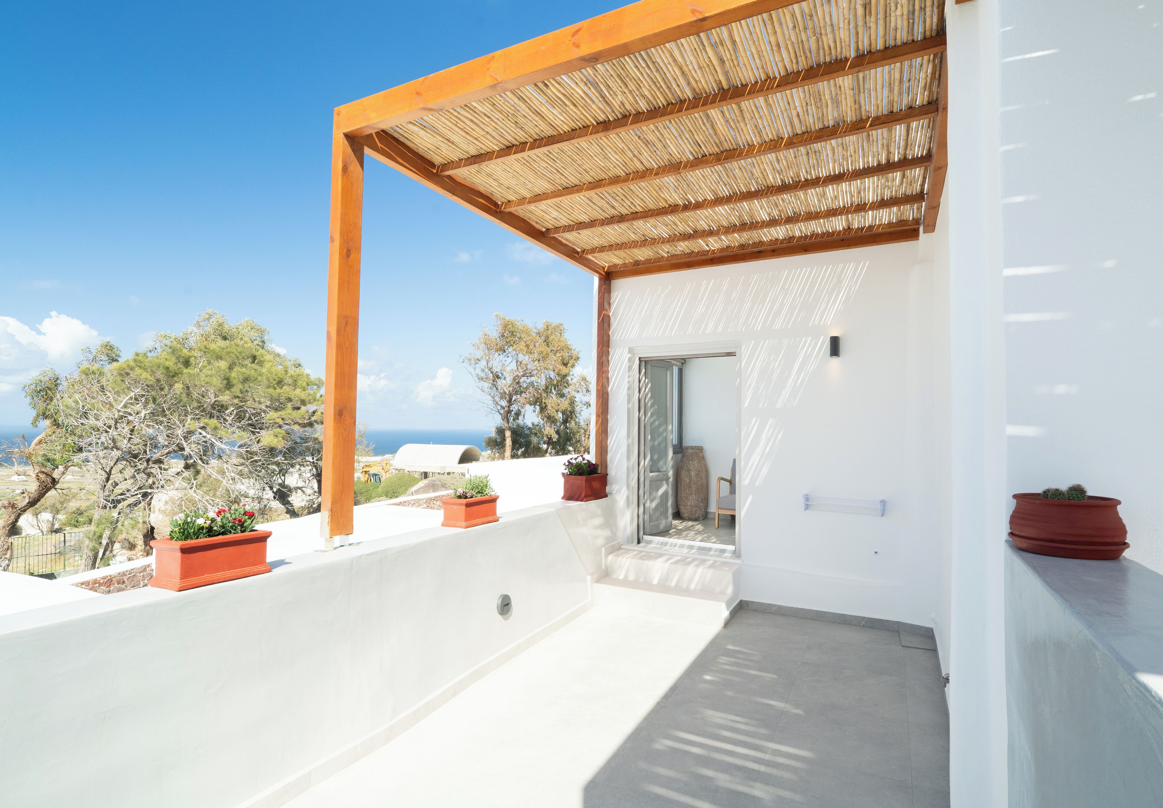 A modern balcony with a wooden pergola, white walls, and potted plants.
