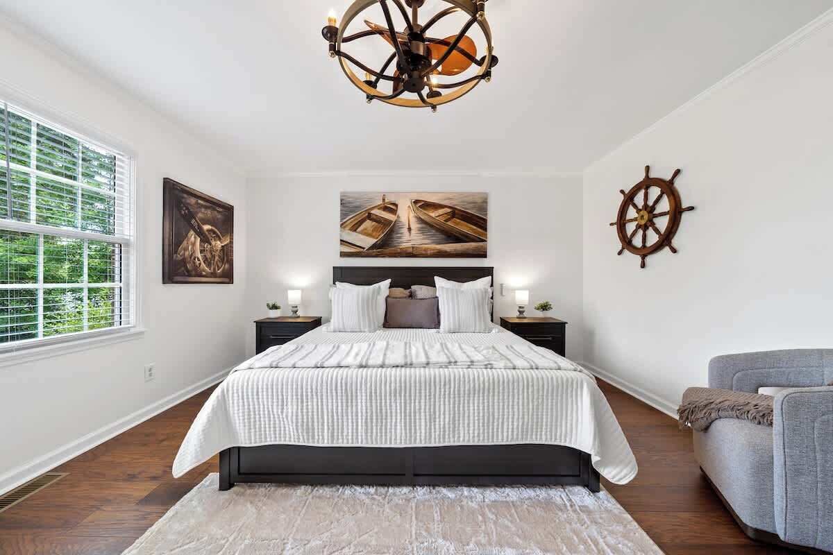 A bedroom with a large bed, a chandelier, a sail wheel decoration, and artwork on the walls.