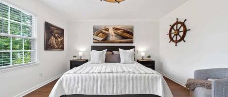 A bedroom with a large bed, a chandelier, a sail wheel decoration, and artwork on the walls.