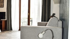 Un salon moderne avec un canapé gris, une petite table ronde surmontée d’une lampe et un téléviseur posé sur un meuble.