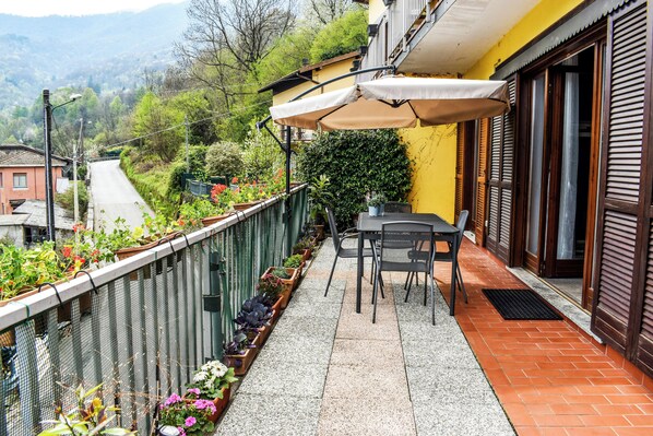 A balcony with a table and chairs, potted plants, and a view of a road and hills. - Casa di Spino (Molina)