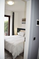 A bedroom with a bed, a nightstand, a lamp, a window with curtains, and a potted plant.