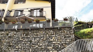 Un mur de pierre surmonté d’une rambarde métallique, un immeuble jaune doté de balcons et un escalier.