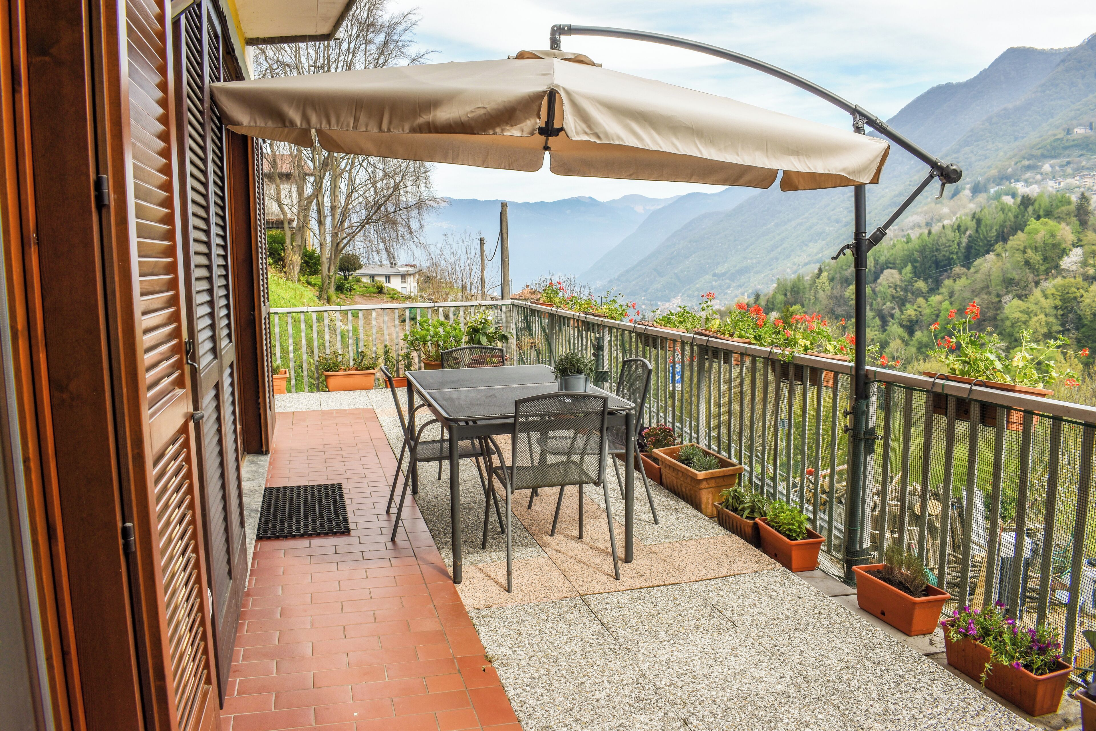 A balcony with a table and chairs, potted plants, and a view of mountains.
