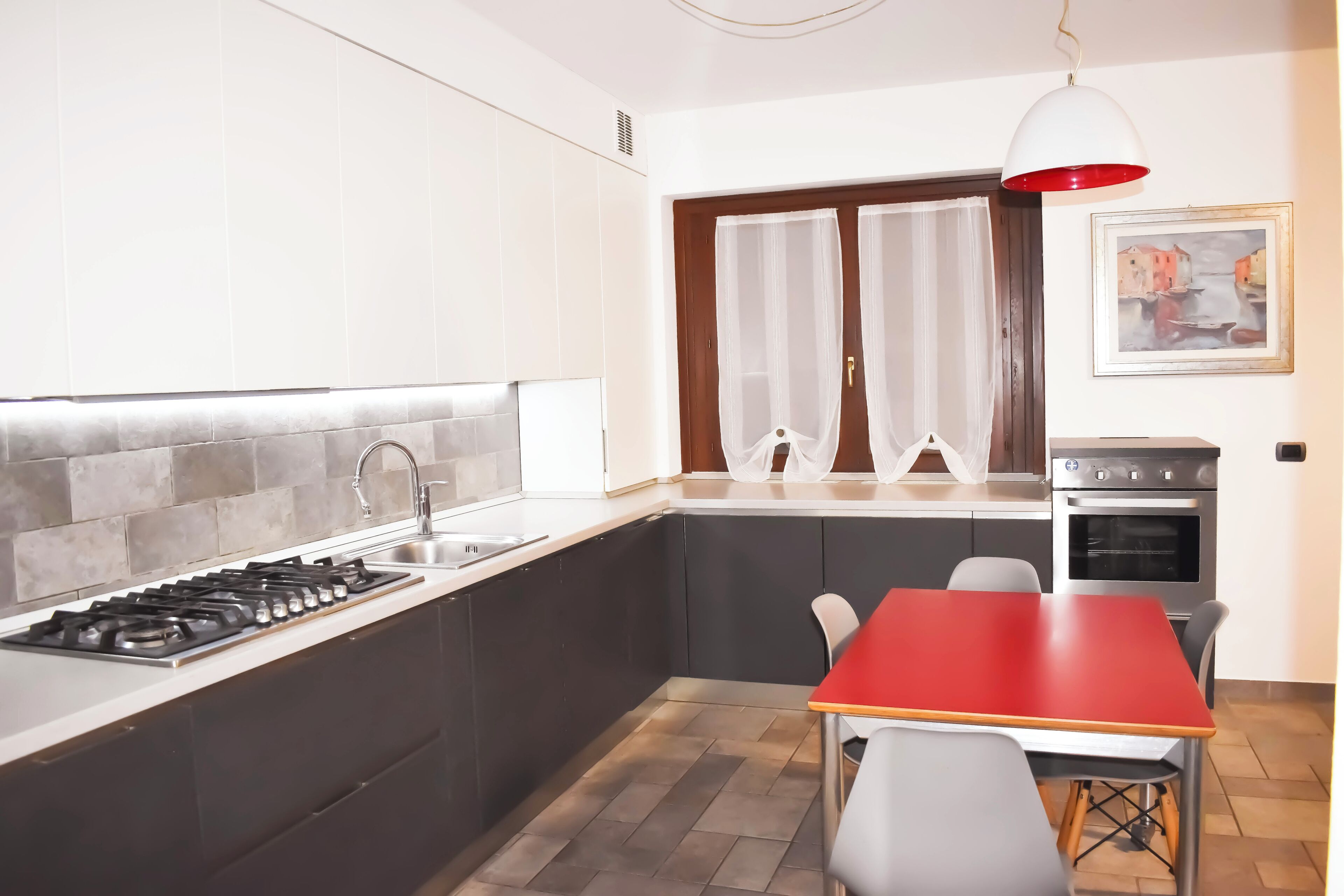 A modern kitchen with a gas stove, sink, and a dining area with a red table and chairs.
