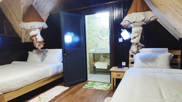 Un acogedor dormitorio en el ático con dos camas, piso de madera y un baño a la vista a través de una puerta abierta.