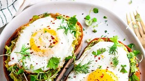 Dos tostadas cubiertas de aguacate, huevos pochados y adornadas con hierbas.