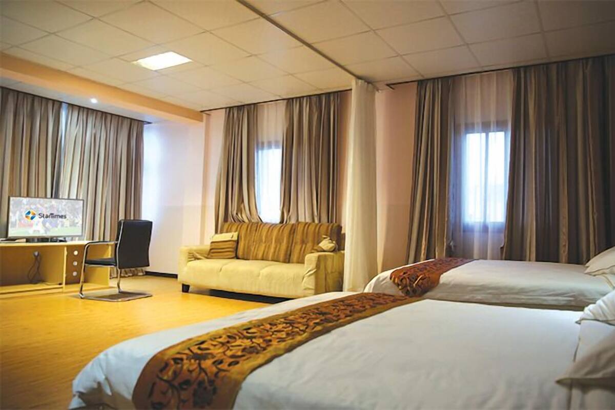 A hotel room with a bed, a sofa, a desk with a computer, and curtains.