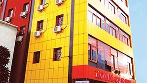 Un hotel de varios pisos con fachada amarilla y roja, unidades de aire acondicionado y un letrero que indica que es un hotel.