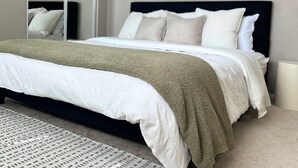 A neatly made bed with a white and green blanket, a dark headboard, and a mirror on the wall. - Modern 2-Bedroom Condo Prime Location (Rancho Cucamonga)