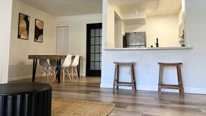 A modern kitchen with a stainless steel refrigerator, wooden stools, and a dining area with a table and chairs. - Modern 2-Bedroom Condo Prime Location (Rancho Cucamonga)