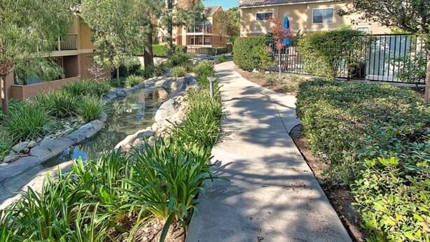 A residential area with a paved walkway, a small water feature, and various plants. - Modern 2-Bedroom Condo Prime Location (Rancho Cucamonga)