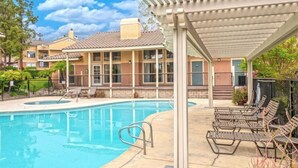 A swimming pool with lounge chairs and a covered area, surrounded by residential buildings. - Modern 2-Bedroom Condo Prime Location (Rancho Cucamonga)